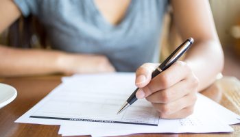 Close-up of woman filling application form in cafe. Unrecognizable young woman working with papers. She busy with documents. Paperwork concept